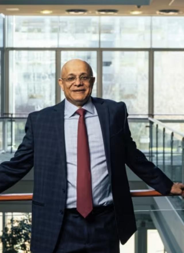 photo of a man in glasses, leaning against a balcony