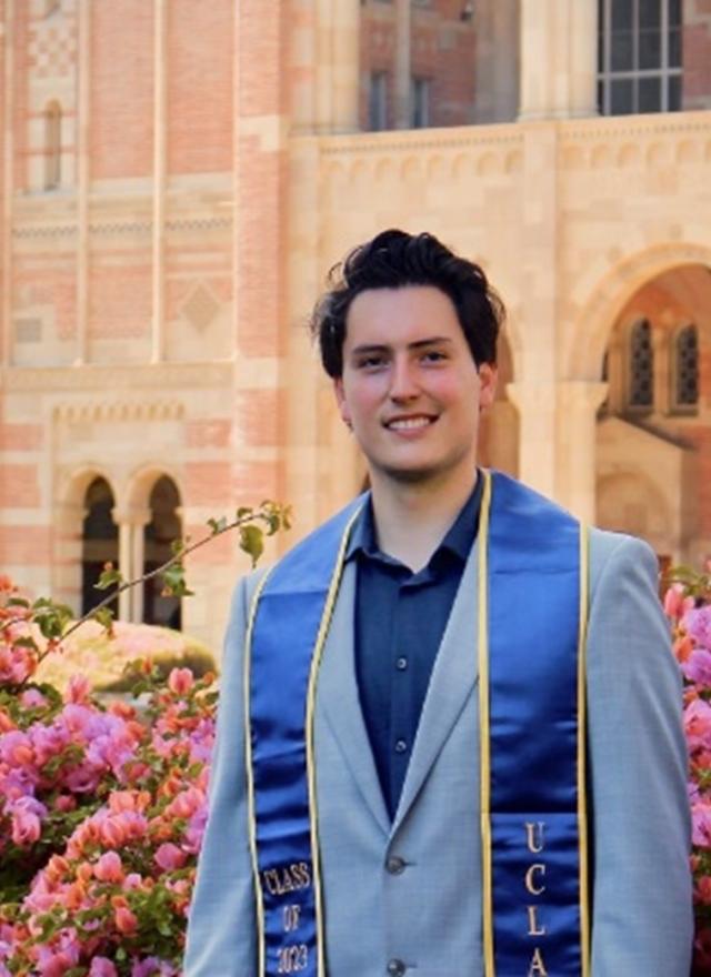 Gabe Fernandez standing in a garden on UCLA campus, wearing a graduation stole