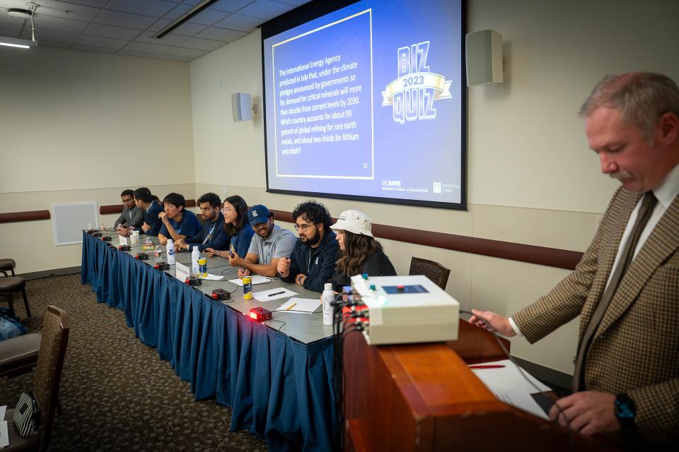 Participants sit at a table with buzzers with the moderator standing near to ask quiz questions